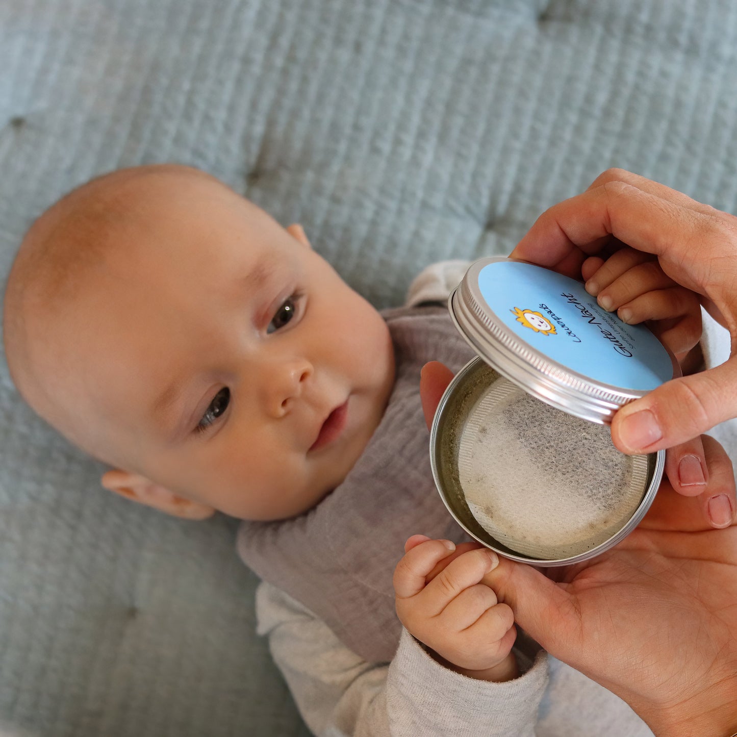 Baby mit grauem Musselin-Halstuch und Kräuterpad-Dose
