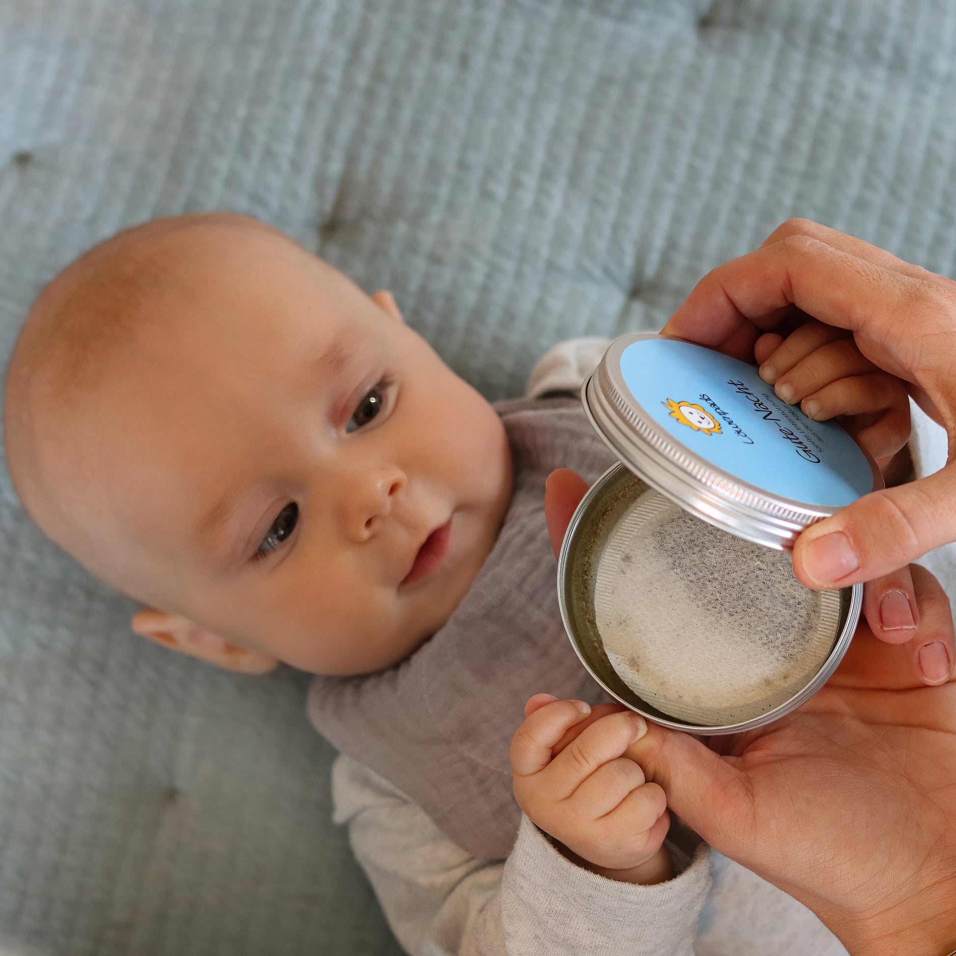 Baby mit grauem Musselin-Halstuch und Kräuterpad-Dose